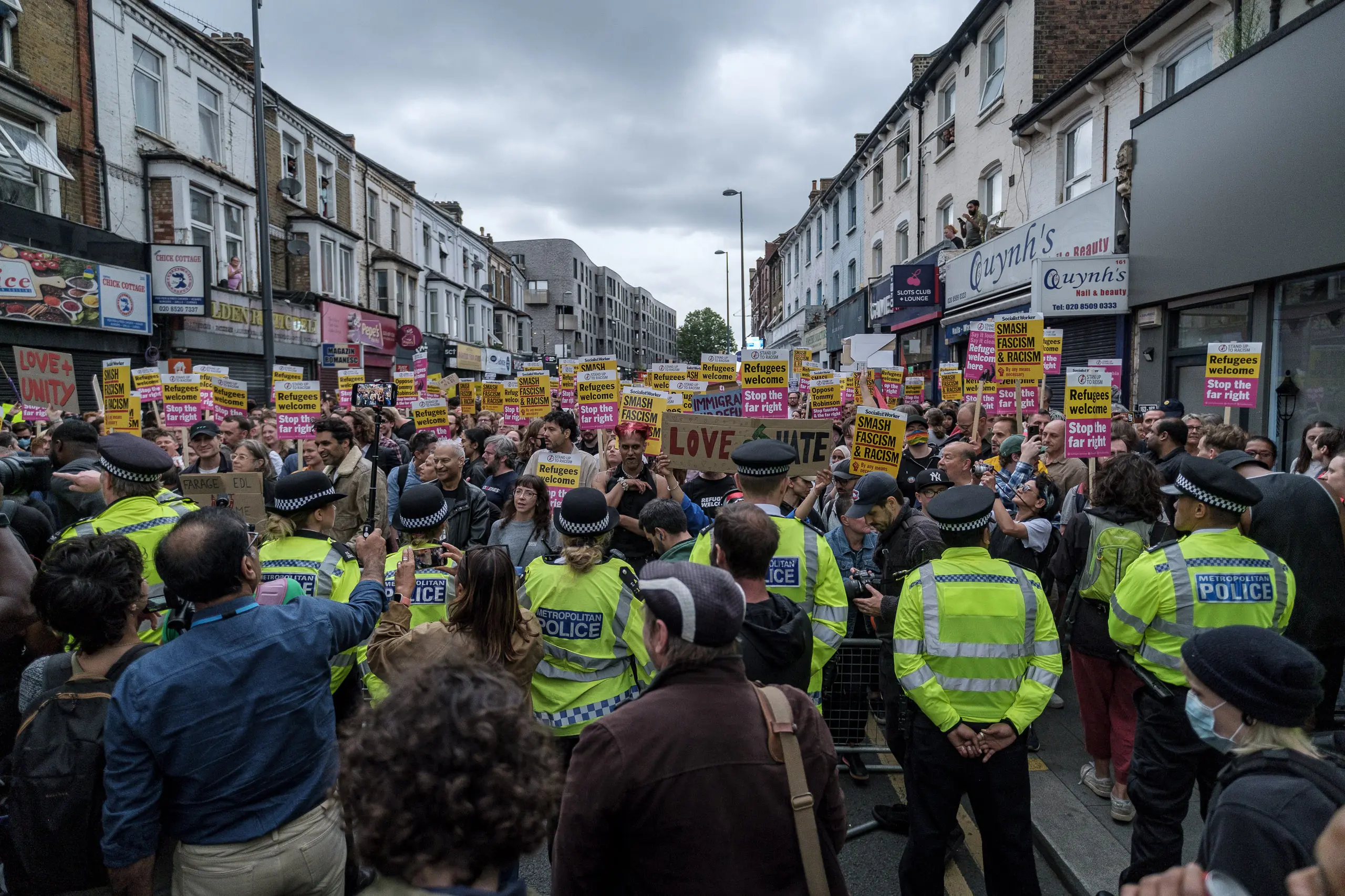 Protestors hold anti-racist signs before a line of police in Hi-Vis. On the night of August 7, 2024 in Walthamstow, North-East London, a gathering of over 10,000 people put paid to a wave of racially motivated riots that had swept the UK for nearly two weeks, targeting Muslims, parts of the asylum system and the police. Similar anti-racist protests happened in Birmingham, Brentford, Brighton, Bristol, Newcastle and North Finchley.