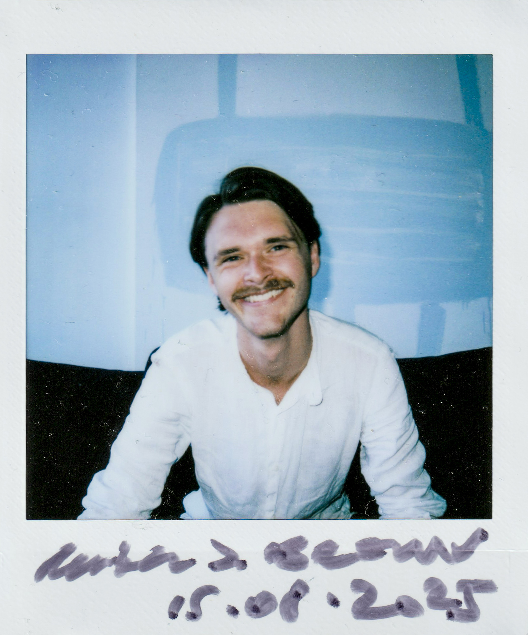 Headshot ofReuben J. Brown against blue background, hard flash, polaroid